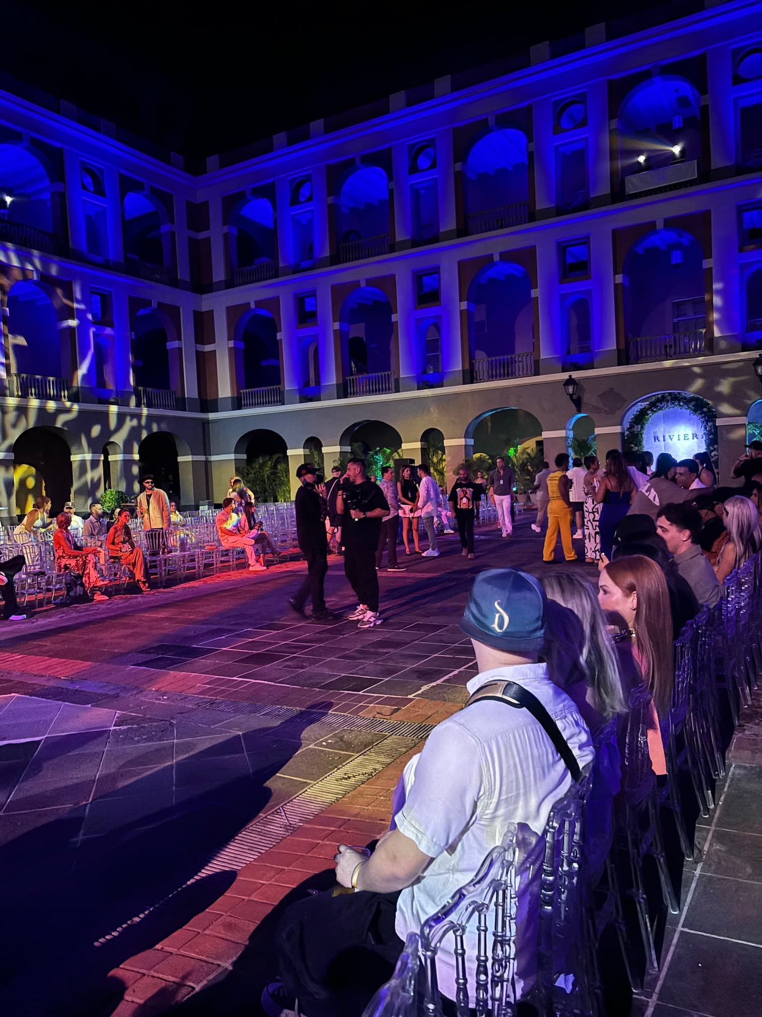 Guests gathered at a nighttime event in a historic courtyard lit in blue and violet